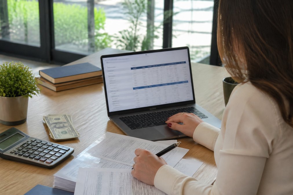 Luxury property manager reviewing occupancy rates and dynamic pricing adjustments on a dashboard across multiple distribution channels, laptop screen visible with graphs and booking data, natural office lighting
