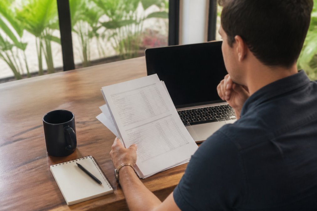 Property owner reviewing financial statements and fee breakdown on a laptop with a coffee cup and notebook on a wooden desk, natural daylight streaming through a window