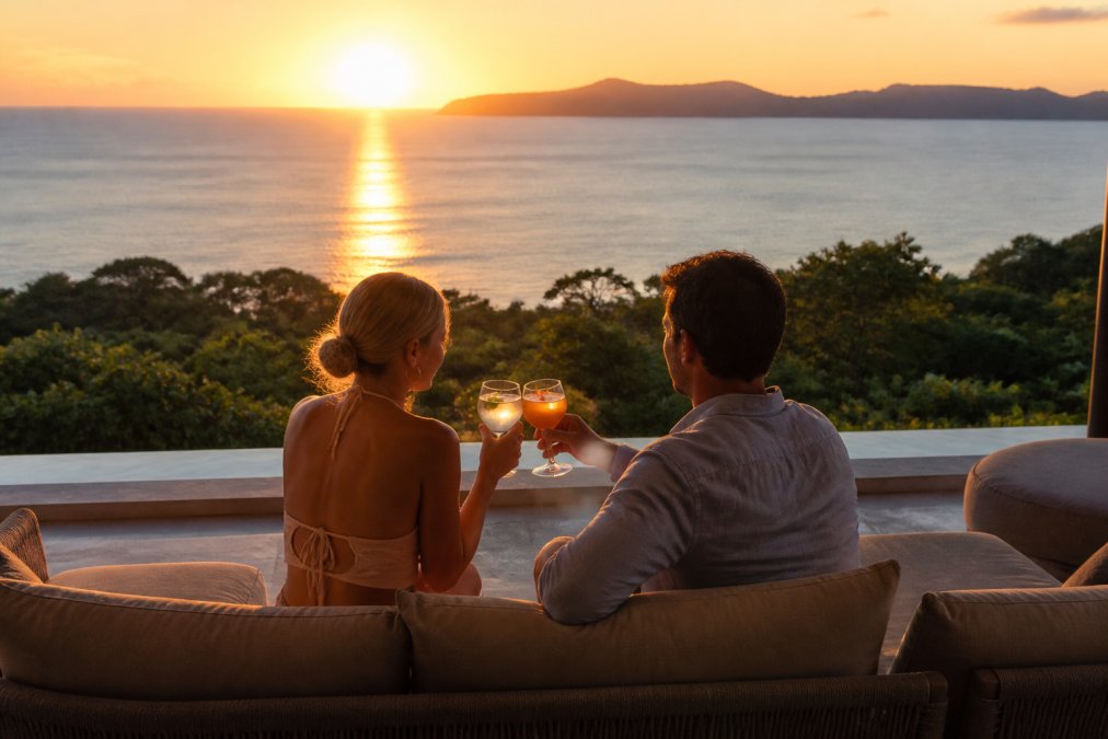 Luxury villa terrace at sunset with a couple enjoying cocktails overlooking the ocean, capturing the exclusive experience that drives repeat bookings