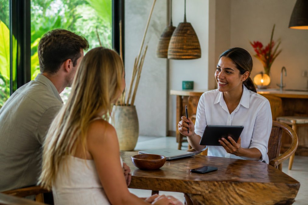 Professional concierge staff member assisting guests at a villa, arranging activities and airport transfers with tablet and phone in hand, bright office setting